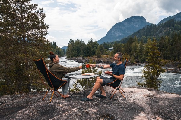 camp life taktelt annie og rob norse camp 2 personer ved elva som setter på hver sin camp stol med bord i mellom norse camp