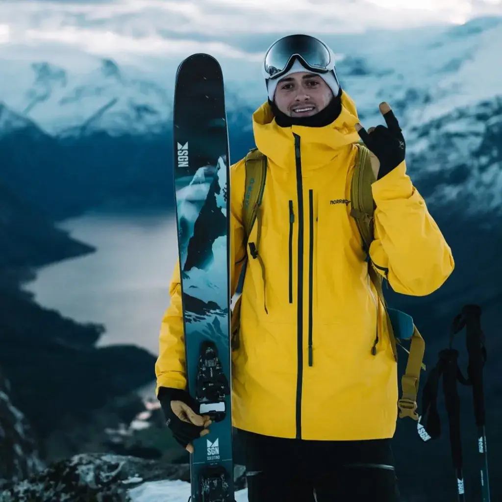 skiløper med ski og gul jakke i fjellandskap